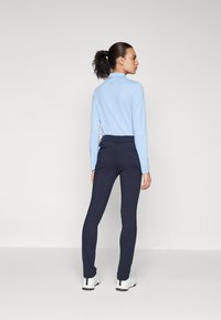 Hellblaues Langarmhemd mit strukturiertem Muster, kombiniert mit dunkeln, schmalen Jeans. Die Schuhe sind weiß mit schwarzen Akzenten.