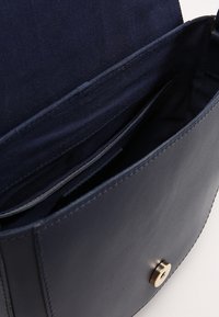 Borsa in pelle blu navy con chiusura a scatto dorata, dotata di interno in tela e diverse fessure per carte. Texture liscia, design semplice a scatola.
