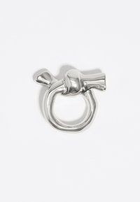 Anillo de metal de color plateado con forma de un ave estilizada. Presenta una textura lisa y brillante con una abertura redonda y un acento en forma de ave en la parte superior.