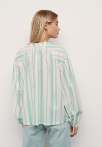 Blouse ample en blanc, ornée de rayures verticales vert menthe et gris clair. Tissu doux avec des manches bouffantes et un détail froncé au dos.