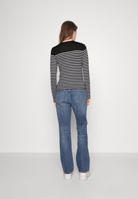 Haut à manches longues rayé noir et blanc avec une silhouette ajustée, associé à un jean évasé bleu et des chaussures à plateforme blanches.