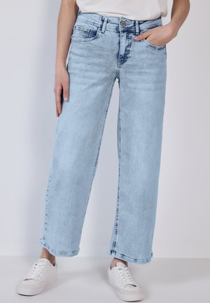 Jean large bleu clair en denim, avec taille haute, décoloration subtile et design classique à cinq poches, associé à des baskets blanches.