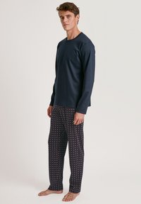 Marineblauwe longsleeve top gecombineerd met pyjamabroek met een geometrisch patroon in rood en wit op een donkere achtergrond. Zacht materiaal.