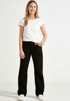 Svarta vida jeans av bomull, kombinerade med en enkel vit T-shirt med kort ärm och vita sneakers, stående mot en neutral bakgrund.