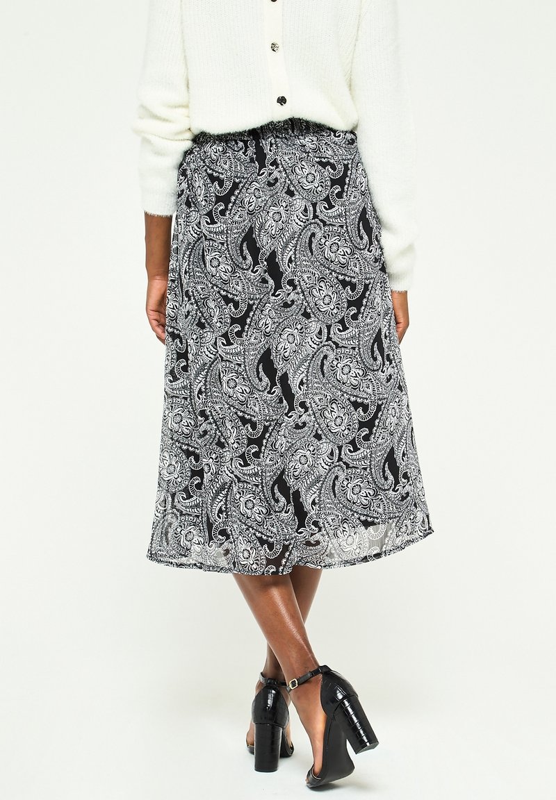 Jupe midi paisley noir et blanc avec une taille élastique, texture transparente et un design fluide, assortie de talons noirs à lanières.