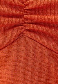 Tessuto arancione a coste con un leggero luccichio metallico, caratterizzato da dettagli arricciati e un design a forma di V al centro.