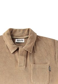 Beige pikétröja i mjukt tyg med krage, kort knappslå och bröstficka. Har en liten märkesetikett på fickan.