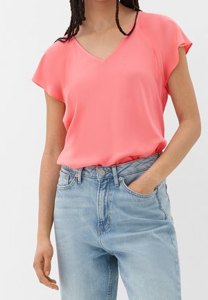 Person wearing a coral short-sleeve V-neck blouse tucked into high-waisted light blue jeans with one hand in pocket.