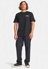 Musta puuvillainen t-paita, jossa on värikäs vuoristografiikka vasemmalla rinnassa, yhdistetty tummiin housuihin ja mustiin tennareihin.