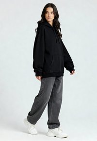 Felpa nera con cappuccio e tasca frontale, abbinata a jeans grigi larghi e sneakers bianche. Tessuto morbido e vestibilità rilassata.