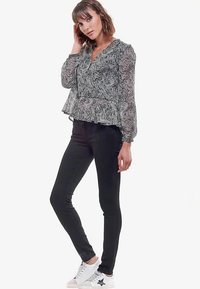 Blouse à motifs noir et blanc avec un ourlet volanté, manches longues en voile transparent, associée à un jean skinny noir et des baskets blanches ornées d'une étoile noire.