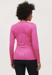 Langærmet atletisk top i lys pink. Glat, strækbart stof med en tætsiddende design. Reflekterende logo-detalje på ryggen og ærmeakcenter.
