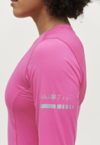 Langærmet atletisk top i klar pink stof med et sølv logo på venstre arm og diskrete syninger. Glat tekstur.
