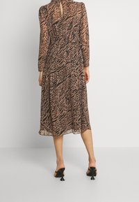 Midiklänning i genomskinligt, lätt tyg med brun och svart djurmönster. Har långa ärmar och en nyckelhålryggdetalj.