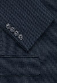 Granatowy blazer z teksturowanej tkaniny z wyraźną kieszenią i czterema ciemnymi guzikami przy mankiecie, z detalicznym przeszyciem.