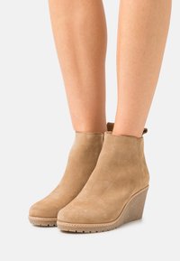 Stivaletti alla caviglia wedge in suede beige con punta arrotondata, suola in gomma texturizzata e un piccolo loop sul retro per un facile indosso.