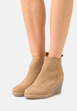Bottines à talons compensés en daim beige avec un bout arrondi, une semelle en caoutchouc texturé et une petite boucle à l'arrière pour un enfilage facile.