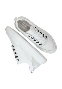 Witte sneakers met een slank ontwerp, gemaakt van leer en suède, zwarte oogjes en witte veters. Voorzien van een textuurlijke zool en een trekband.