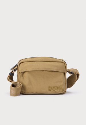 Tan crossbody taske med et tekstureret stof, hovedrum med lynlås, frontlomme og præget logo. Justerbar rem, kompakt rektangulær form.