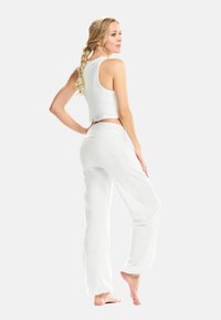 Top corto bianco e pantaloni bianchi larghi, realizzati in materiale morbido, con una texture liscia e una silhouette rilassata.