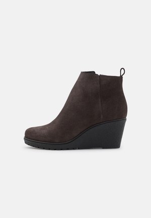 Bottine en daim marron foncé avec talon compensé noir et languette de tirage sur fond clair uni.