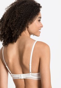 Witte bh met verstelbare bandjes en een haak-en-oogsluiting. Heeft een gladde stof met subtiele horizontale strepen langs de band.