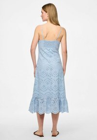 Gaiši zila, bez piedurknēm, vidēja garuma kleita ar acu izšuvumu un ģeometrisku malu. Iespējas ir plāni siksniņas un pieguļošs augšdaļa.