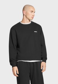 Czarna bluza z okrągłym dekoltem i długimi rękawami, z białym logo "PROSTO." na lewej piersi, w zestawie z czarnymi spodniami.