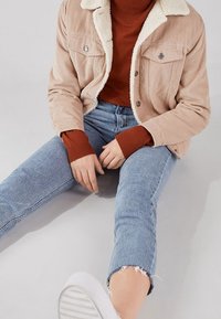 Giacca di velluto a coste con un colletto in pelliccia sintetica, abbinata a un maglione color ruggine e jeans azzurri a taglio corto con orli sfrangiati. Sneakers bianche.