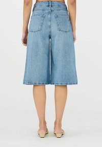 Farmernadrág fazonú culotte, világoskék, közép hosszúságú, hátsó zsebekkel és nyers szegéllyel; magas derekú és laza fazonú.