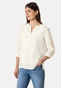 Witte, lichte blouse met een ronde hals, placket met drie knopen en driekwartmouwen. Zachte stof met een gladde textuur.