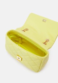 Quiltad gul handväska med en slät yta, med ett guldspänne och kedjedetaljer inuti, som visar en ljus, fodrad insida.