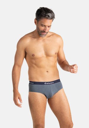 Slip en coton gris avec une ceinture élastique bleu marine portant l'inscription blanche "Eminence". Le tissu semble lisse avec une coupe ajustée.