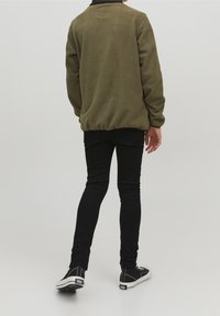 Veste en polaire vert olive avec une coupe décontractée, un col rond et un ourlet élastiqué, associée à un pantalon noir slim et des baskets noires.
