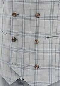 Szary kamizelka w kratę z podwójnym zapięciem, z okrągłymi brązowymi guzikami, dwoma bocznymi kieszeniami oraz wyraźnym, dopasowanym krojem.