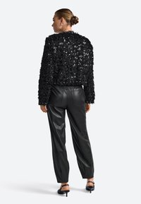 Melnā teksturētā jaka ar pērlītēm, daļēji īsa dizaina, apvienota ar melnām ādas biksēm. Augstpapēžu melnas sandales komplektē izskatu.