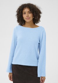 Pull à manches longues bleu clair, en texture douce, avec un large col bateau, associé à une jupe en daim marron foncé avec des poches arrière.