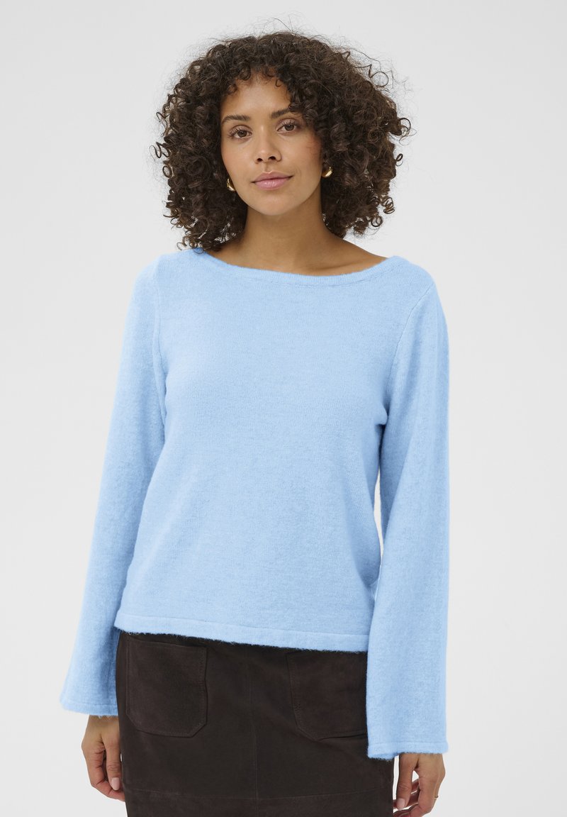 Pull à manches longues bleu clair, en texture douce, avec un large col bateau, associé à une jupe en daim marron foncé avec des poches arrière.