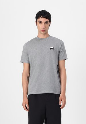 Camiseta de manga corta gris en un tejido suave, con un pequeño gráfico en blanco y negro en el pecho. Bajo recto y escote redondo.