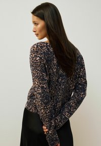 Pull en imprimé léopard dans des teintes de brun et de noir, avec une coupe décontractée, des manches longues et des poignets côtelés, associé à une jupe noire.