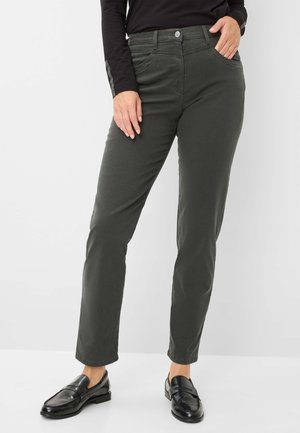 Grüne Baumwollmischungshosen im Slim Fit mit Knopfverschluss, fünf Taschen und subtilen Stickdetails. Kombiniert mit schwarzen Slippern.