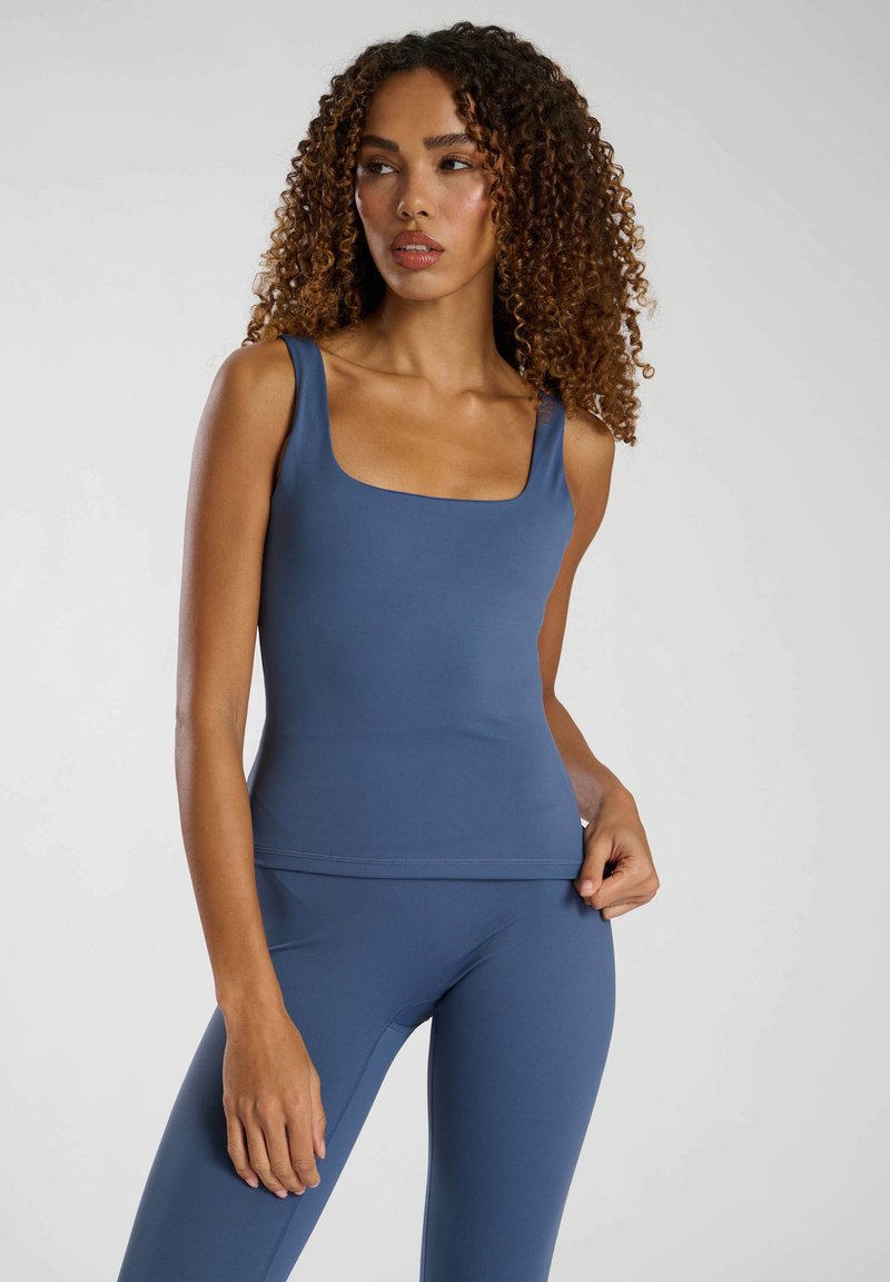 Niebieski dopasowany top bez rękawów z kwadratowym dekoltem, wykonany z gładkiego, elastycznego materiału. W zestawie z dopasowanymi legginsami o wysokim stanie.