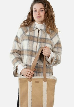 Plaid wool-blend coat in cream and beige, featuring a zipper and wide sleeves. Holding a tan canvas tote with fuzzy cream accents.