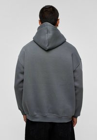Grijze hoodie met een gestructureerde afwerking, ontspannen pasvorm en geribde manchetten. De achterkant heeft een eenvoudige design en een diepe capuchon.