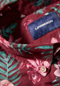 Korte mouwen bordeauxrood shirt met tropisch bloemenpatroon in roze en groen. Voorzien van een knoopkraag en een LINDBERGH-label. Zachte stoftextuur.