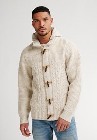 Cardigan crema a maglia con cappuccio, presenta bottoni in legno e polsini a coste, evidenziando un design texture e accogliente.