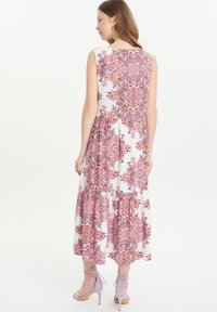 Blumenkleid Maxi mit weißem Grund, pinken und lila Paisleymustern, ärmellosem Design, gestuftem Rock, kombiniert mit helllila Schuhen.