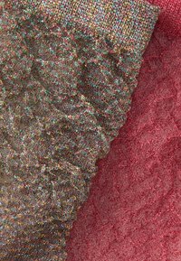 Têxteis com um padrão tecido metálico e multicolorido de um lado e um tecido rosa sólido com uma superfície texturizada e acolchoada do outro.