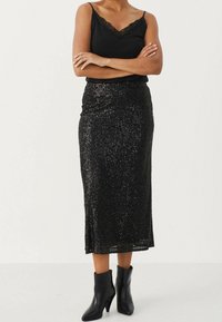 Jupe noire pailletée de longueur mi-mollet et de coupe slim, associée à un débardeur noir avec bord en dentelle et des bottes noires à la cheville.