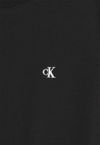 Svart sweatshirt med rund halsringning och en liten vit broderad "cK"-logotyp placerad på vänstra sidan. Mjuk tygstruktur.